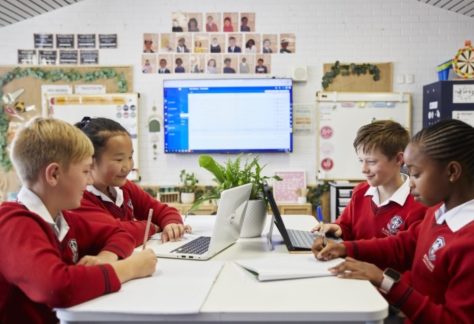 primary school students doing school work on laptops in classroom